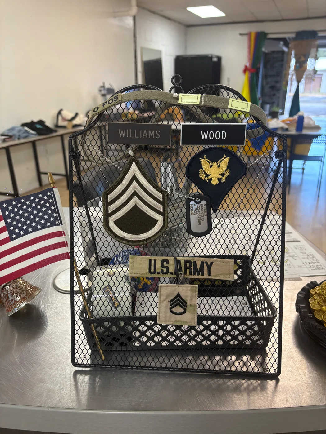 U.S. Army rank patches, name tapes and dog tags displayed in a black wire stand beside a small American flag