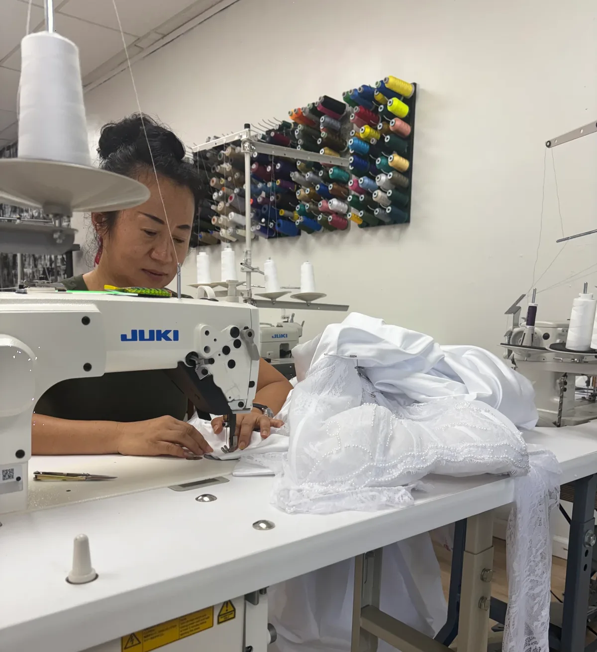 Seamstress at a JUKI sewing machine stitching a white beaded wedding dress in the shop